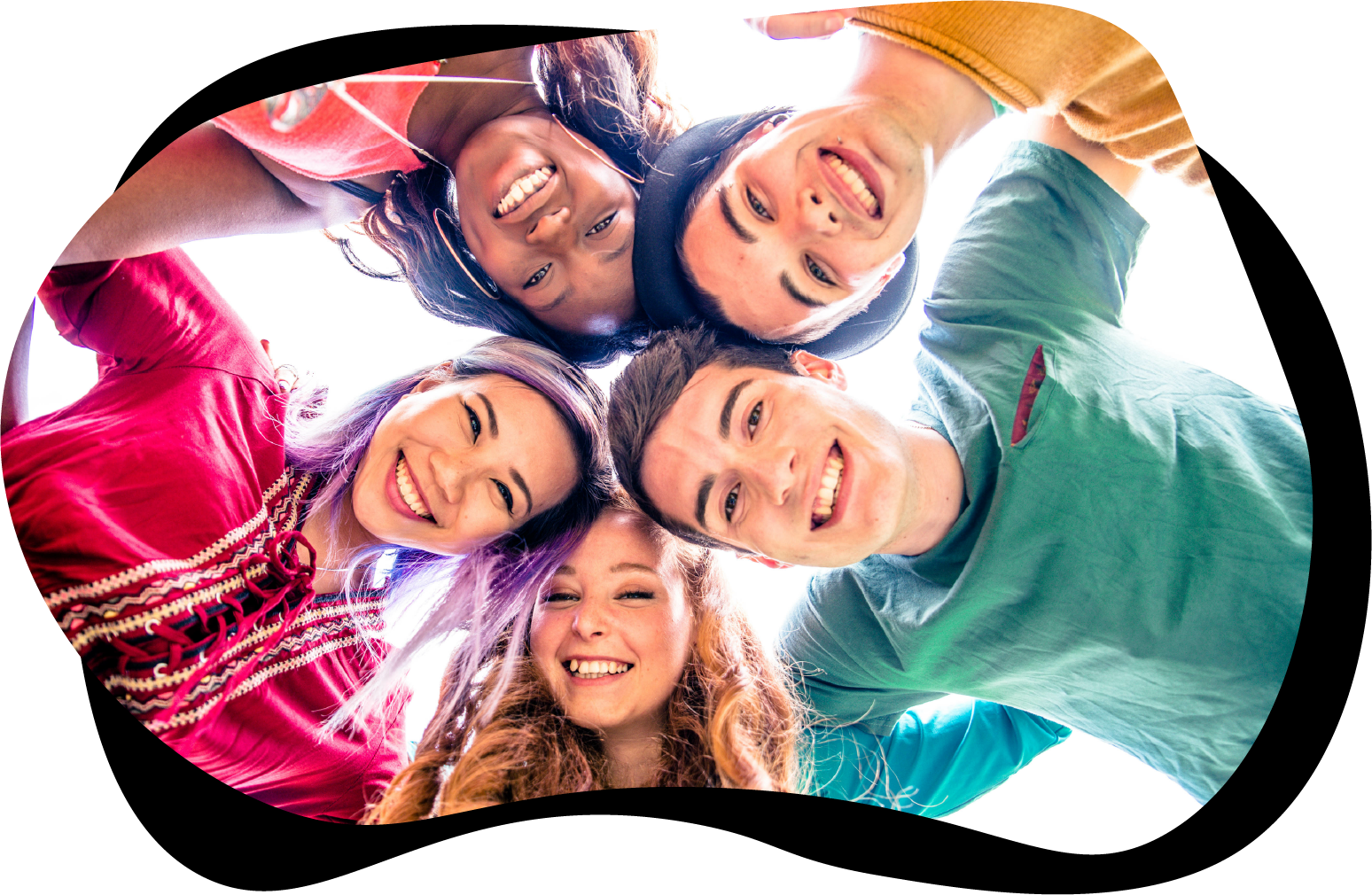 Fem ungdommer som står samlet i en ring og holder armene rundt hverandre, samtidig som de ser ned i kamera. De smiler og har på seg fargerike klær.