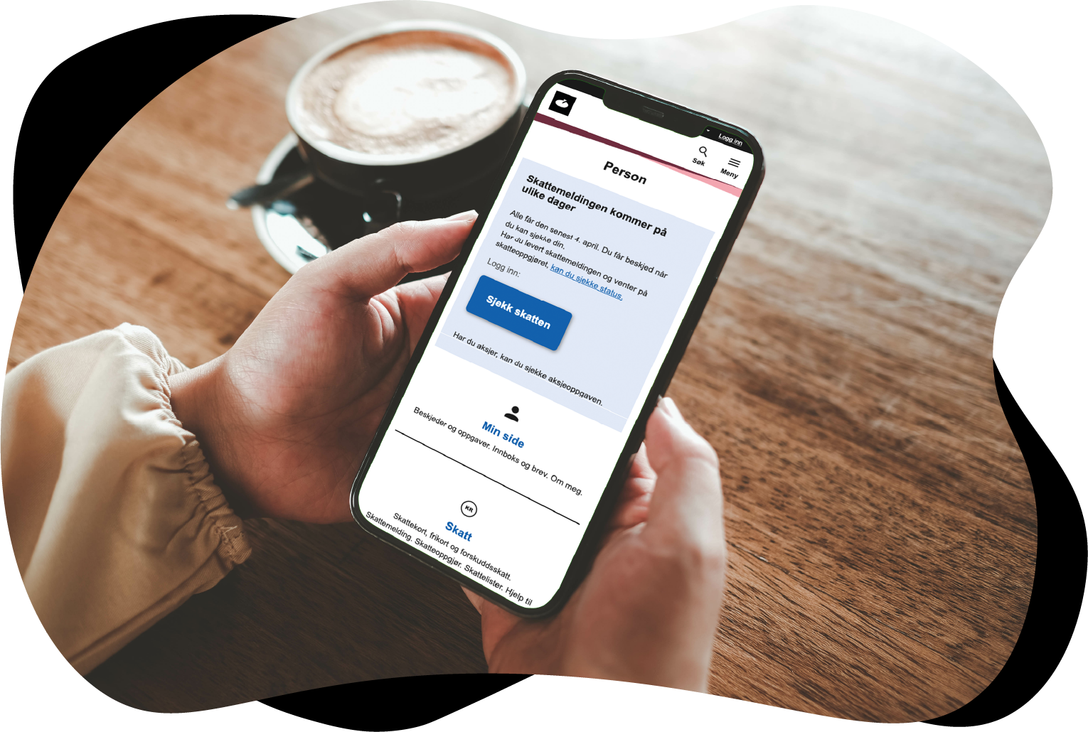 Nærbilde av hender som holder en mobiltelefon. På skjermen ser vi informasjon om skatt. I bakgrunnen står en kaffekopp på et bord. Foto: Thaspol/Adobe Stock.