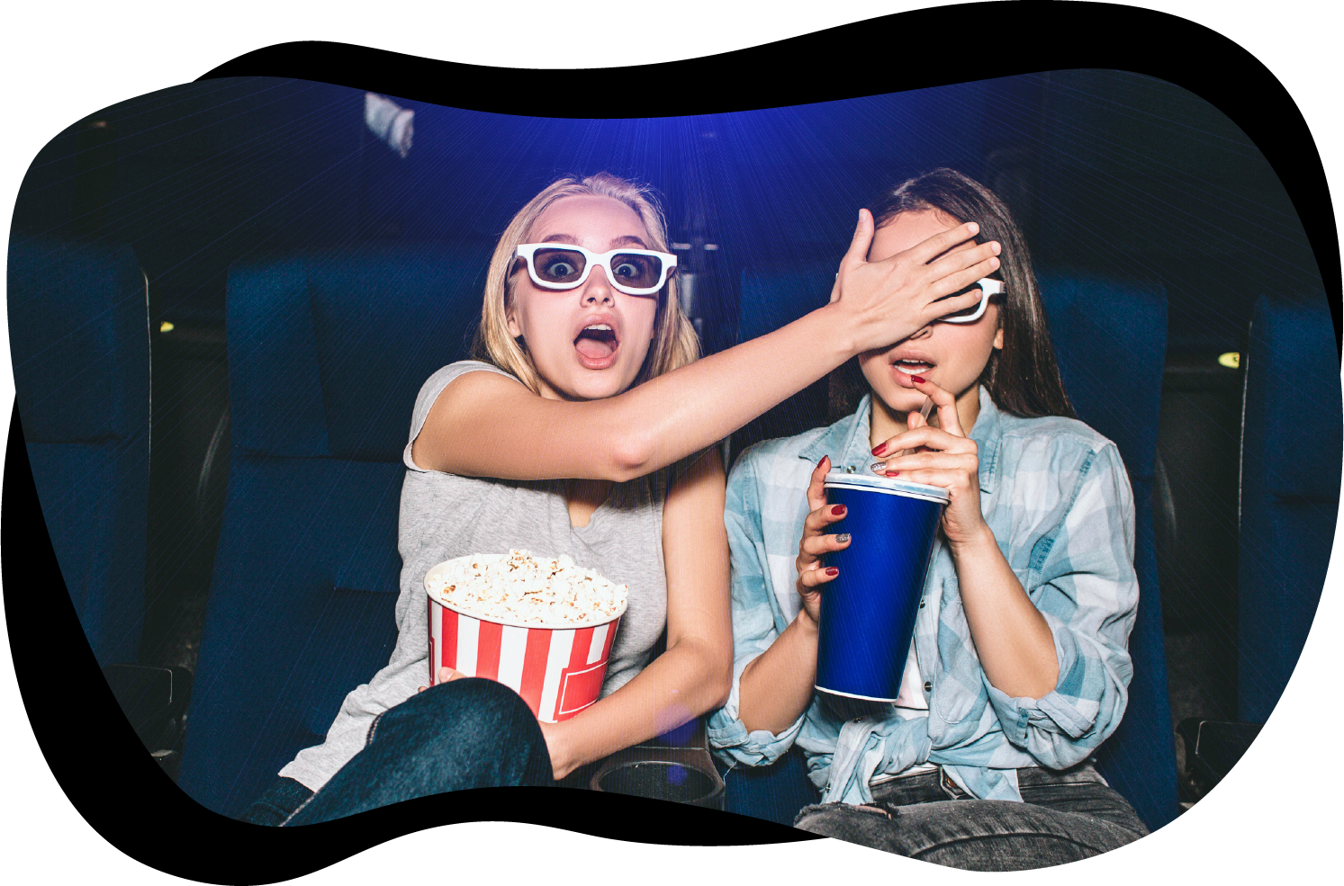 To tenåringsjenter som sitter i en kinosal med popcorn og brus i fanget. De har på seg 3D-briller. Den ene jenta ser forskrekket ut, og holder hånden over øynene til den andre jenta. Foto: Adobe Stock/estradaanton